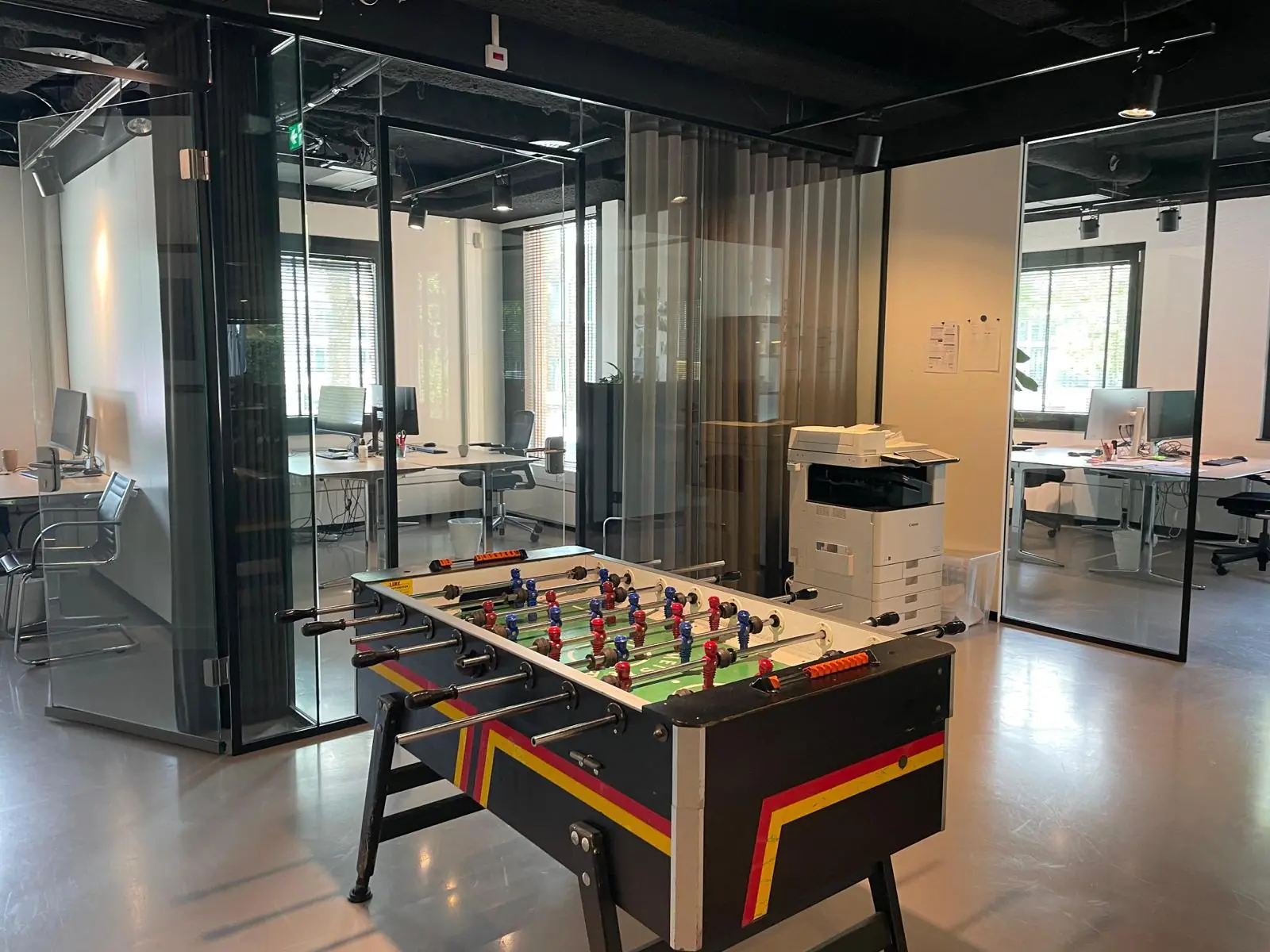 Modern kantoor aan de De Cuserstraat met glazen vergaderruimtes, een tafelvoetbaltafel en een printer.